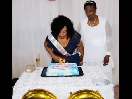 Salome Ogilvie blows out the candles on the cake at her 80th birthday celebration on August 10. Looking on is Janet Nembhard.