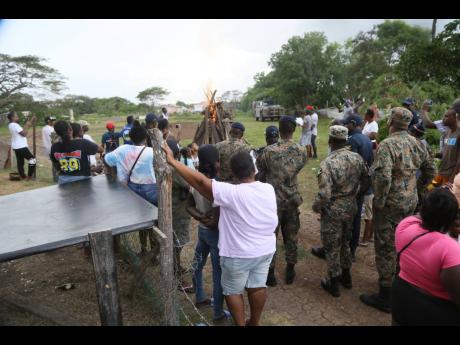 Members of the security forces keep a close eye as residents of Cherry Tree Lane and neighbouring communities in Four Paths, Clarendon, light a bonfire on Friday as part of the healing process following the death of eight persons on August 11. Another 10 m