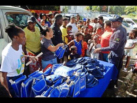 Children gather around the area where school bags were being distributed during last Thursday’s health fair and treat, as personnel from Sandals and the St Ann police get ready to start handing them out.