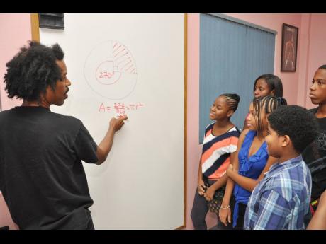 Samuel McDaniel (left) shows how to solve a maths problem to 13-14 year old students.