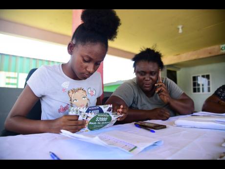 Sue-Anne Shakes (left) and Tamieka Blake sort through back-to-school vouchers to be distributed at the office of Portland Western Member of Parliament Daryl Vaz.