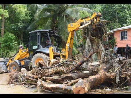 Residents watch as a tractor cleans up debris yesterday after flooding caused by heavy rainfall in John’s Hall in St James on Saturday.