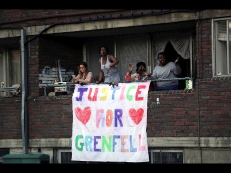 People watch from a balcony as people walk during a demonstration following the fire at Grenfell Towers that engulfed the 24-storey building in London, Friday June 16, 2017.