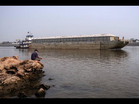 A man fishes on the shore of the Paraguay River where a tugboat pushes a barge amid low water levels and a drought in Mariano Roque Alonso, Paraguay, Monday, September 9, 2024.