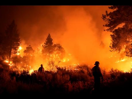 Two firefighters watch the Bridge Fire burn near a structure in Wrightwood, California, on Tuesday.