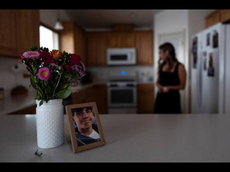 A framed photo of Elijah Ott, who died of a fentanyl overdose at 15, stands next to a vase of flowers as his mother, Mikayla Brown, works in the kitchen in Atascadero, California.