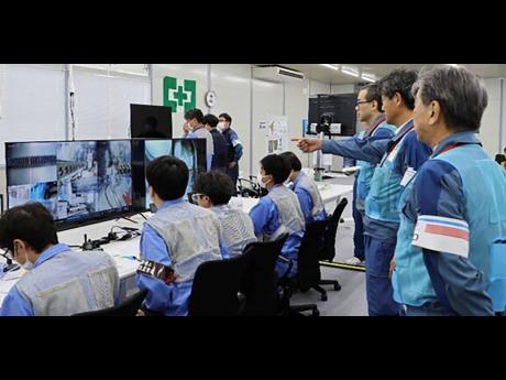 In this photo released by Tokyo Electric Power Company Holdings (TEPCO), TEPCO executives observe a mission to retrieve the first sample of melted fuel debris from inside one of three damaged reactors, at an operation room at the Fukushima Daiichi nuclear 