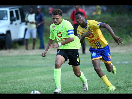 Mona High School’s skipper, Dante Peralto (left) runs away from Tarrant High School’s Giovanni Satchell during their Manning Cup encounter at the Mona playing field yesterday.